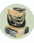 Two handmade soap bars stacked on top of each other, featuring a marbled swirl pattern of cream, black, and gray. The top bar is standing upright, showing the detailed swirled texture, while the bottom bar is resting horizontally.