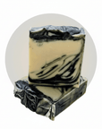 Two stacked rectangular bars of handmade soap with a cream-colored base and black marbled swirls, set against a white background with a light gray circular backdrop.